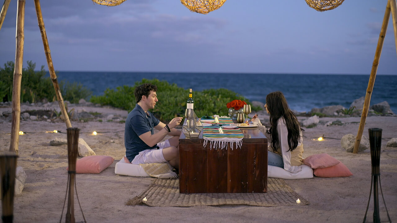 Zack Goytowski and Irina Solomonova sit at a table for dinner on a beach on 'Love Is Blind' Season 4.