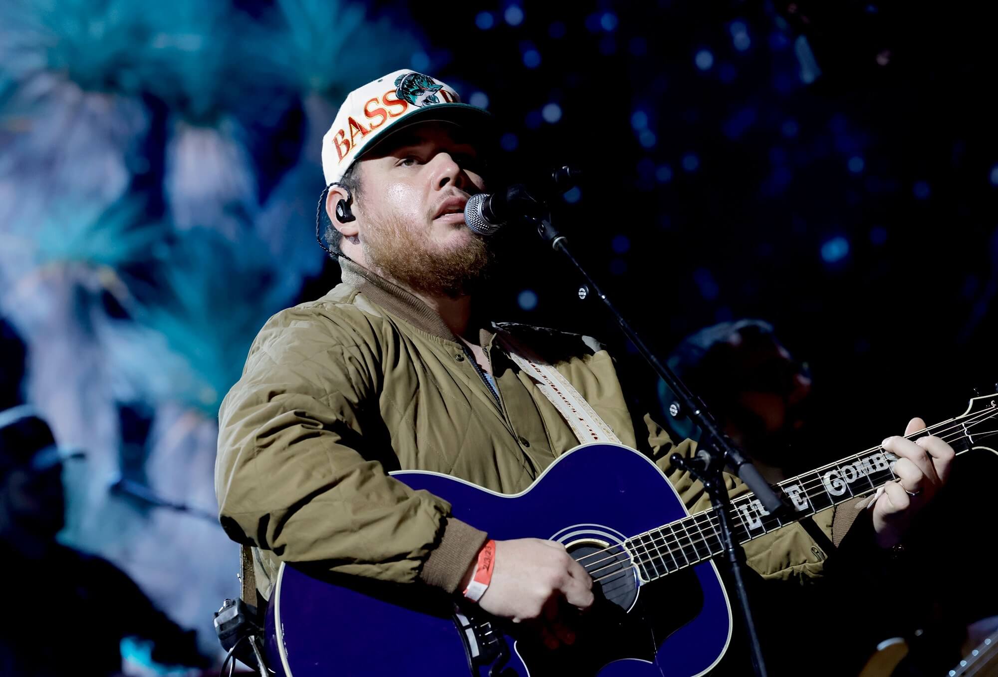Luke Combs sings into a microphone while playing a blue acoustic guitar