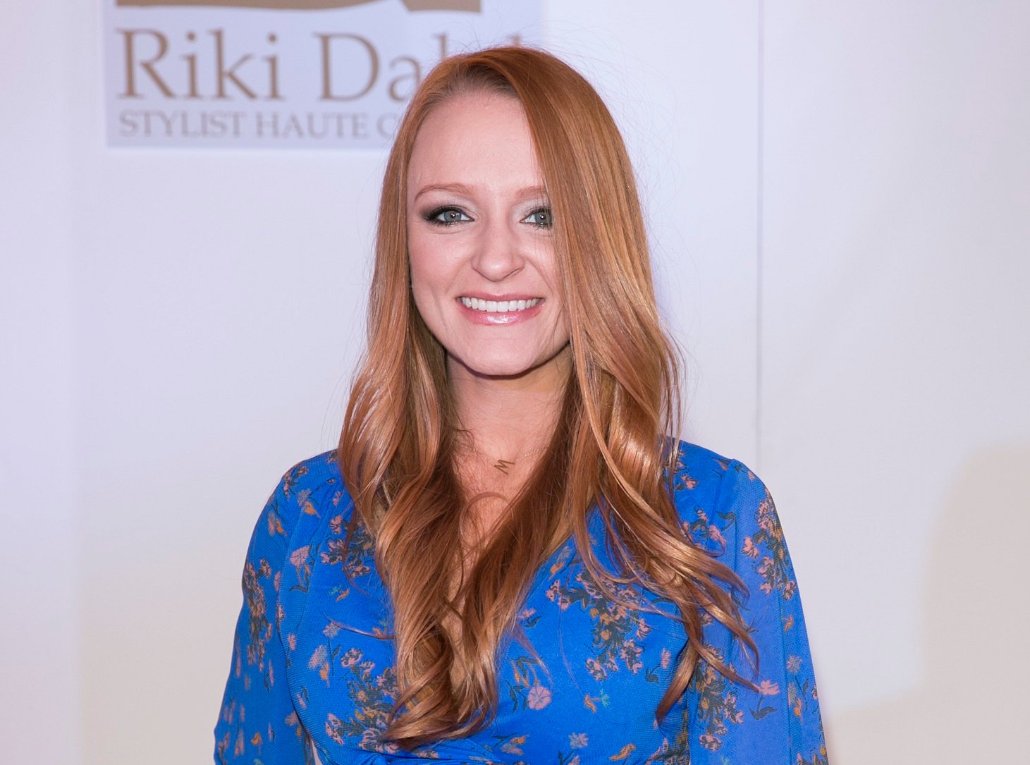 Maci Bookout smiles at the camera while wearing a blue dress with flowers on it