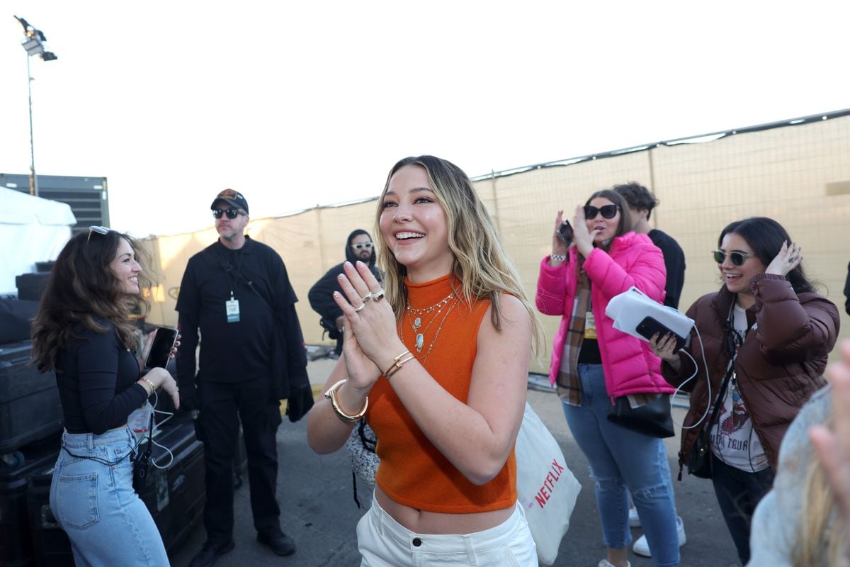 Madelyn Cline smiles while walking around an event with fans taking pictures in the background.