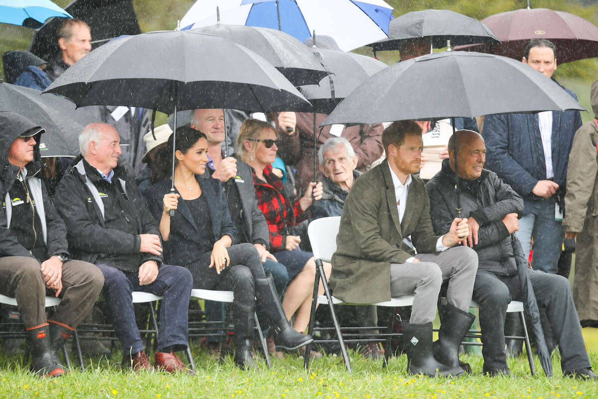 Meghan Markle holds an umbrella during a 2018 royal tour while sitting next to Prince Harry 