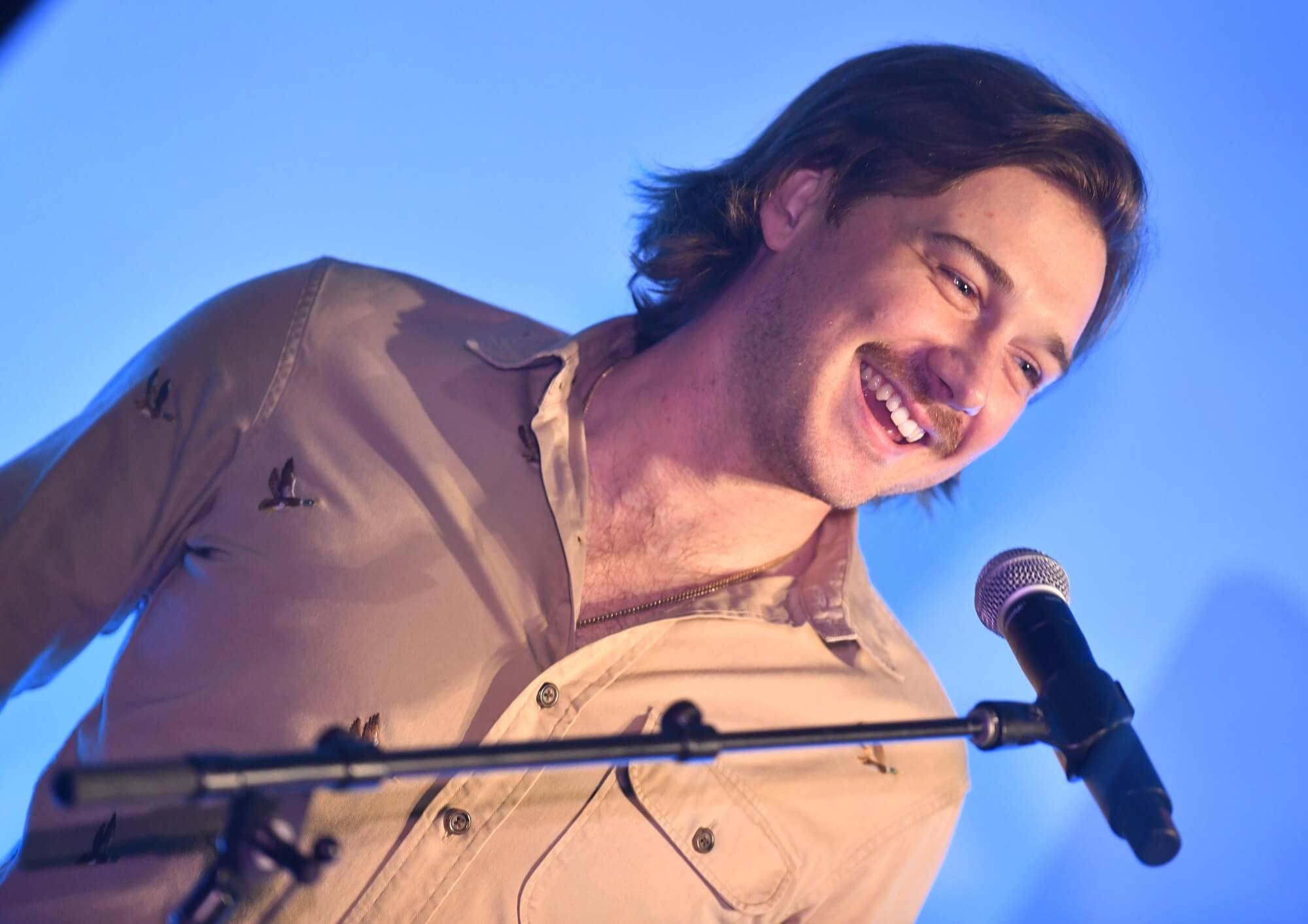 Morgan Wallen smiles in front of a black microphone and microphone stand