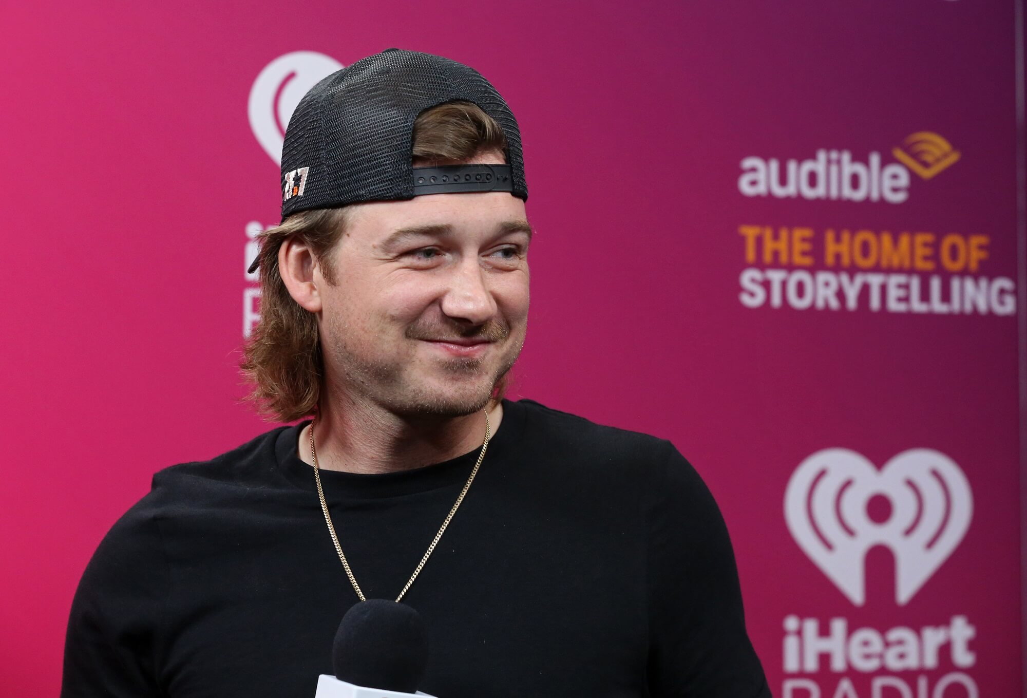 Morgan Wallen wears a black shirt and a black backward baseball cap