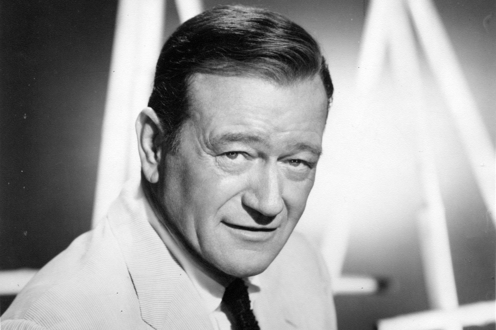 Movie star John Wayne wearing a suit and tie in a black-and-white picture with a slight smile