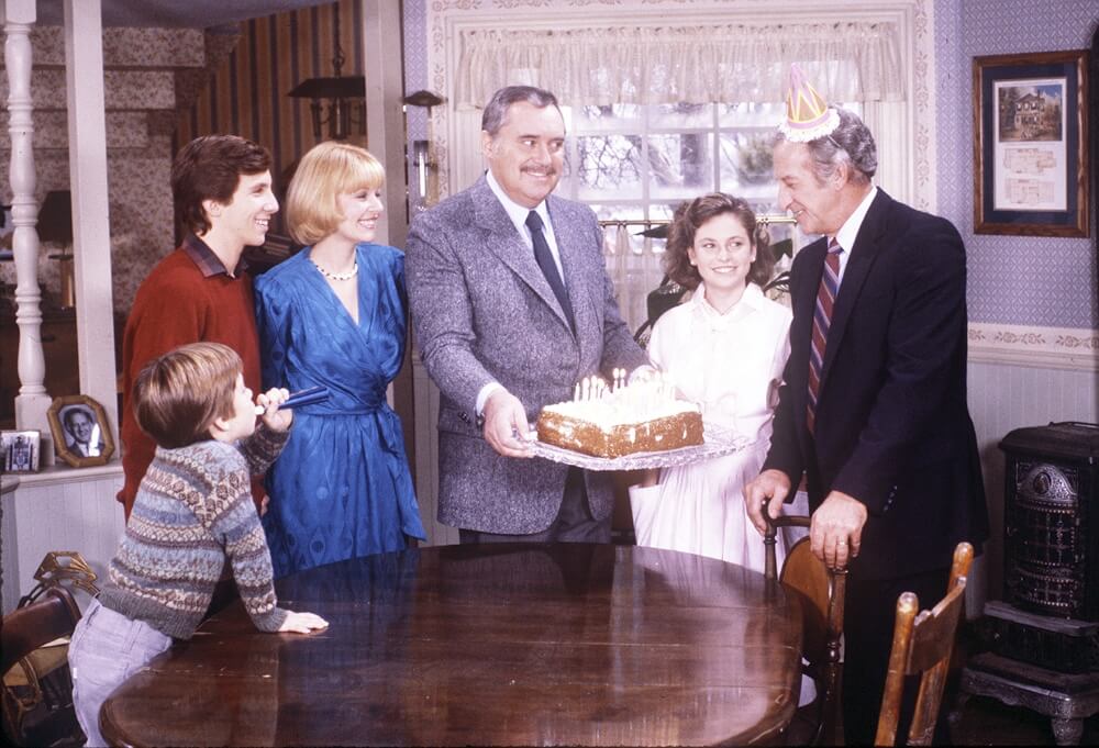 The cast of 'Mr. Belvedere' standing around a cake in the pilot episode