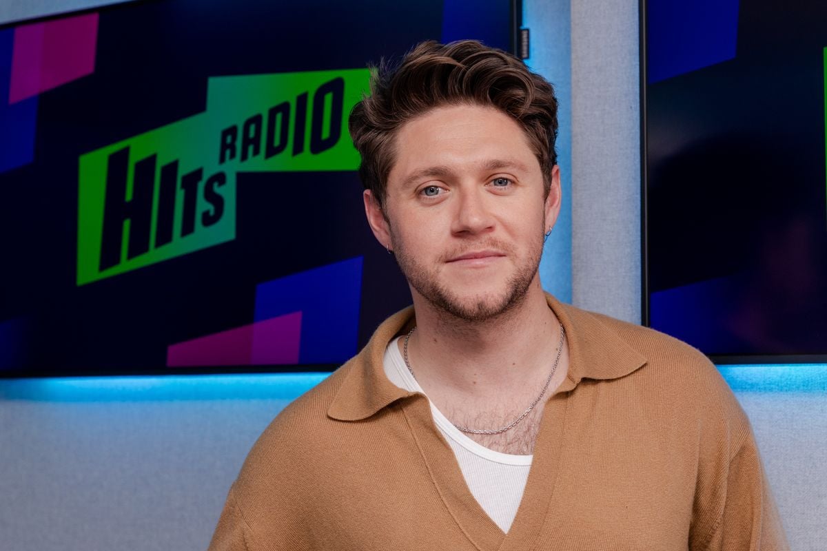 Niall Horan poses for a photo in front of the Hits Radio logo.