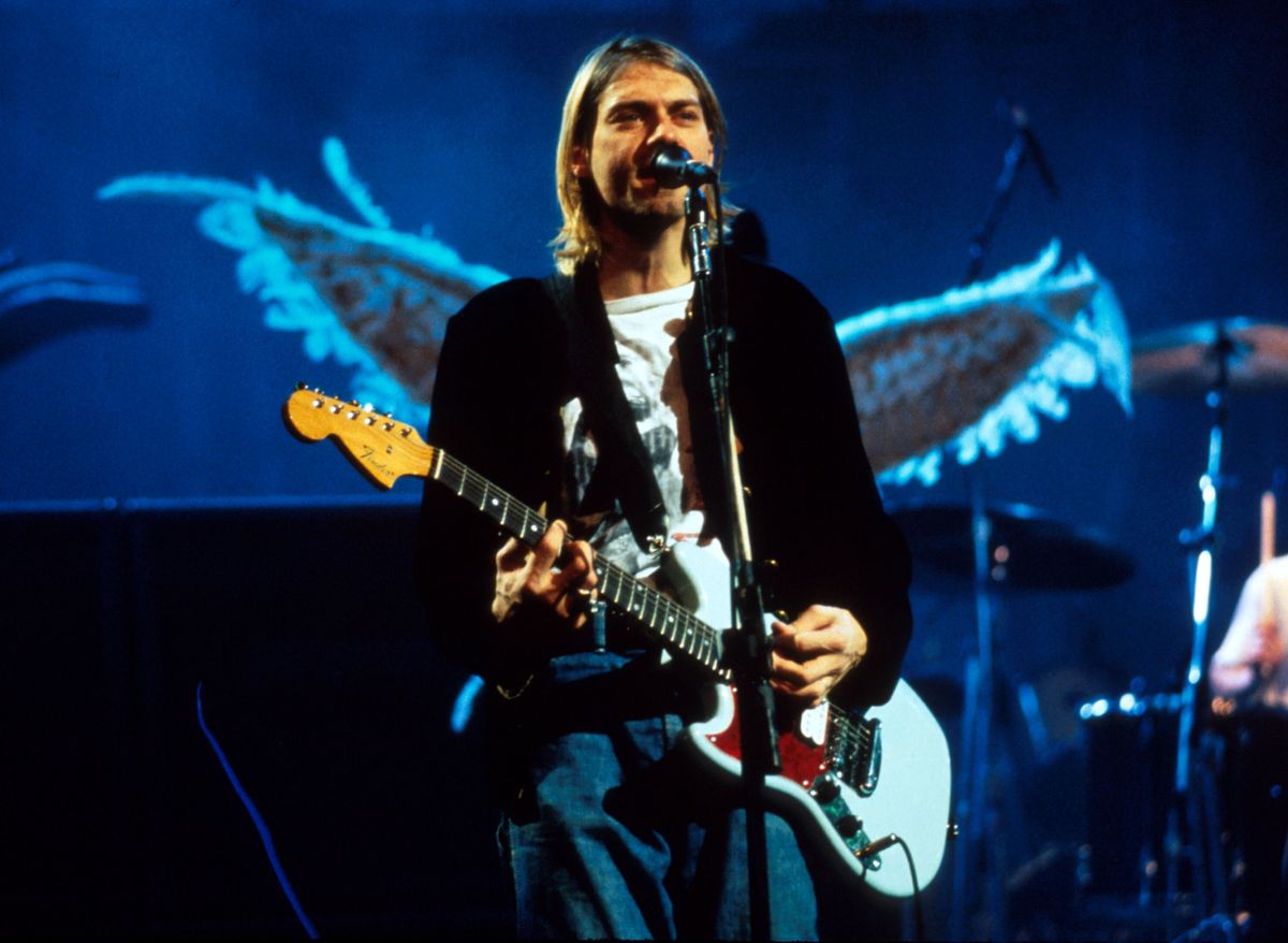 Kurt Cobain of Nirvana plays guitar and sings into the microphone.