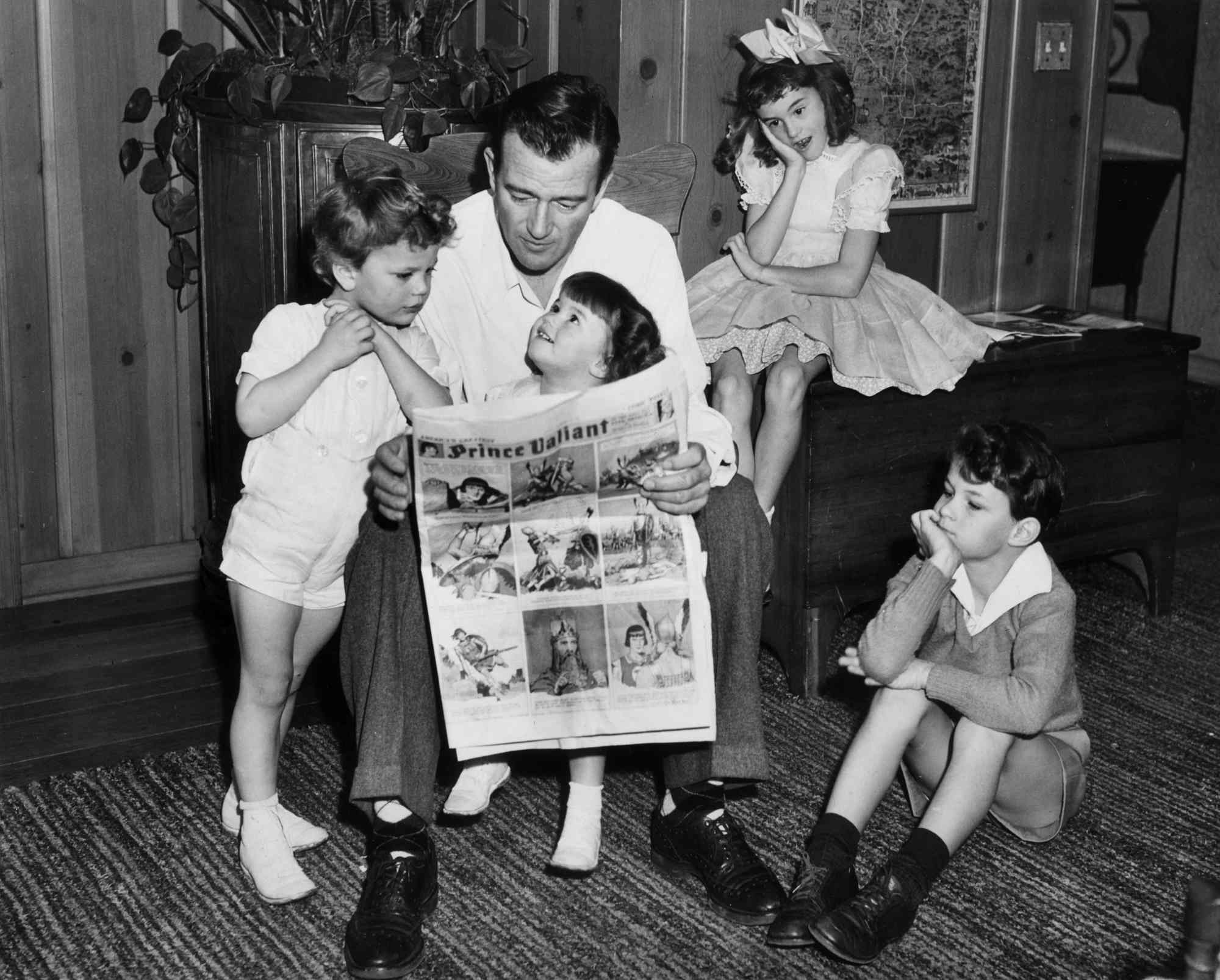 Occasional television guest star John Wayne, along with children Patrick, Melinda, Toni, and Michael. Patrick and Melinda are leaning on their father, while the other two are at the desk and on the floor.