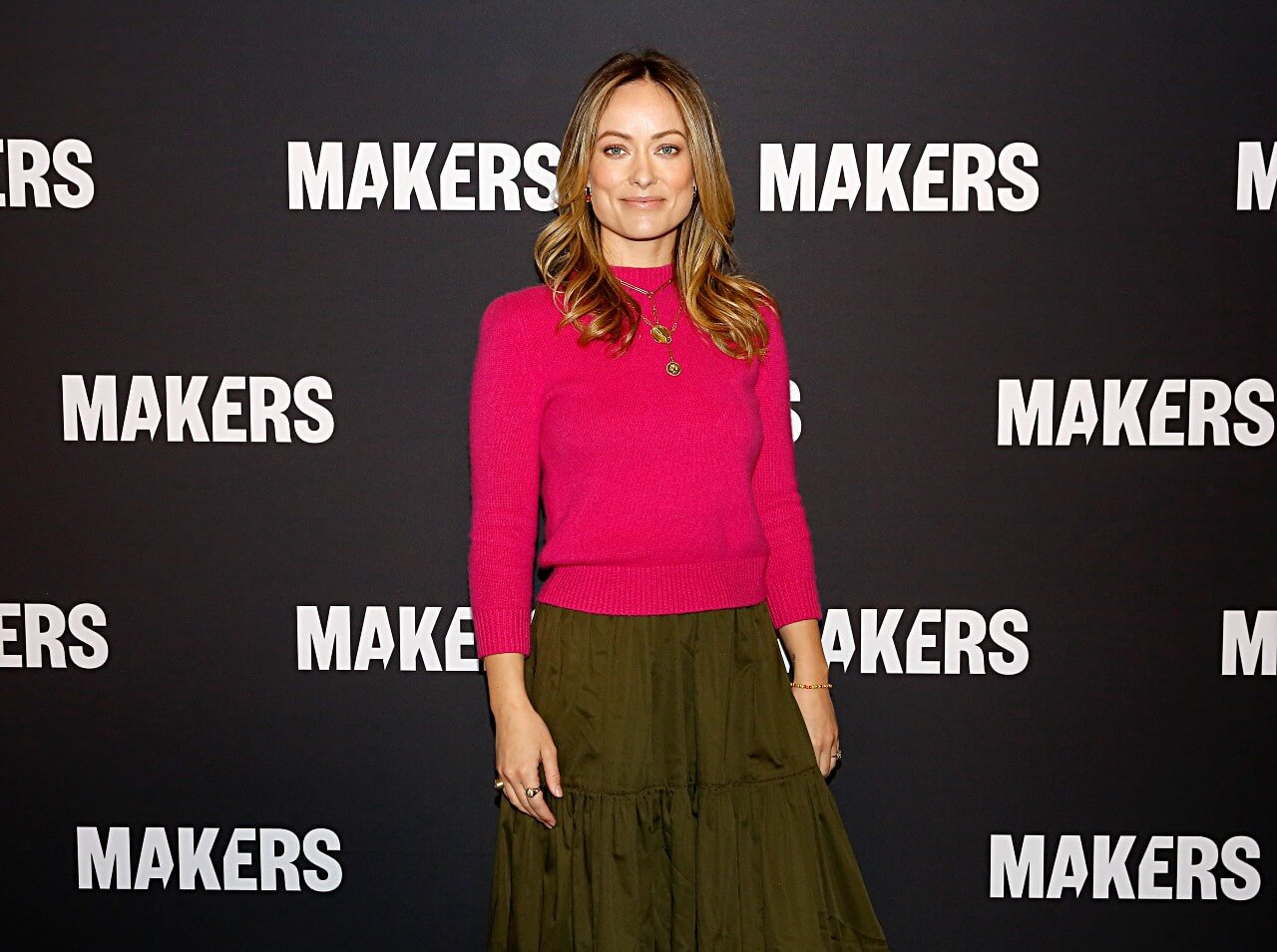 Olivia Wilde wears a red sweater and long skirt while attending an event.