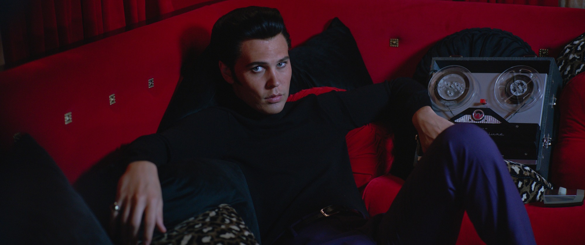 Oscars 2023 Best Picture nominee 'Elvis' Austin Butler as Elvis Presley laying back on a red couch.