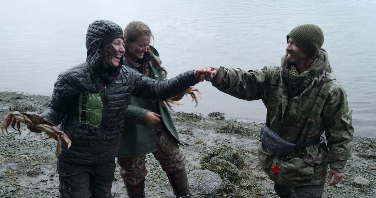 Amber Asay holds a crab by a river with Jill Ashock and Justin Court on 'Outlast'.