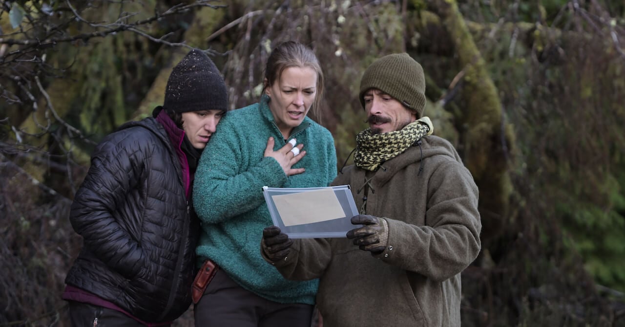 Amber Asay, Jill Ashock, and Justin Court stand together and look at a piece of paper on 'Outlast'.