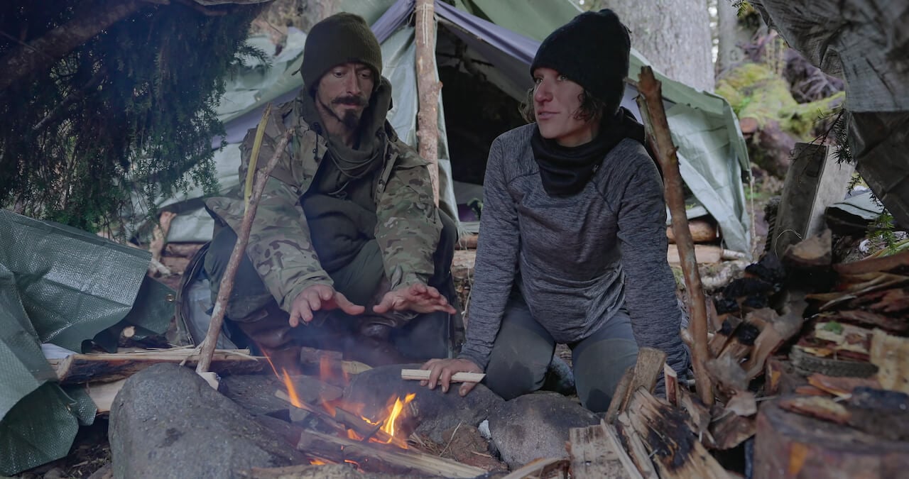 Justin Court and Amber Asay sit in front of a fire under a tarp on 'Outlast'.