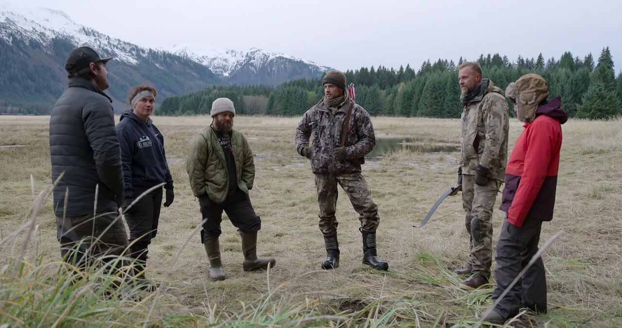 Nick Radner, Dawn Nelson, Seth Lueker, Jordan Williams, Paul Preece stand in a circle in a grassy field on 'Outlast'.