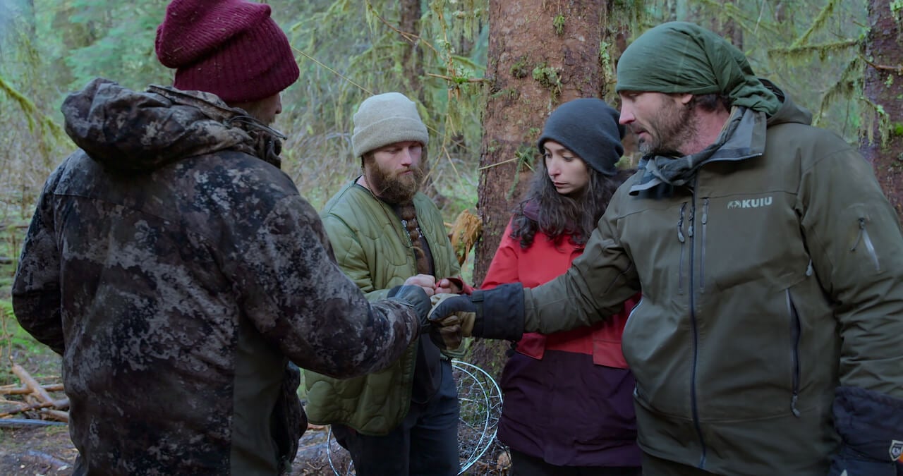 Paul Preece, Seth Lueker, Angie Kenai, and Nick Radner stand in a circle and fist bump on 'Outlast'.