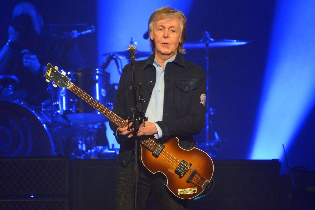 Former Beatles bassist Paul McCartney stands onstage with a bass guitar.