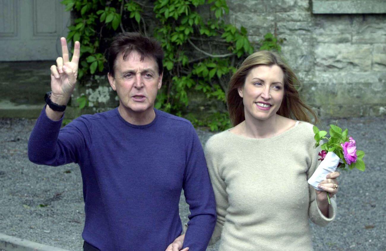 Paul McCartney holds up a peace sign and holds hands with Heather Mills, who holds flowers.