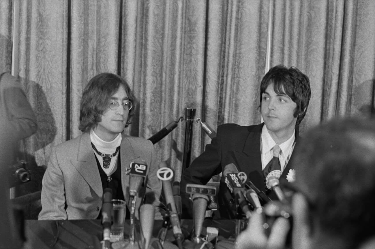 A black and white picture of John Lennon and Paul McCartney sitting in front of microphones at a press conference.
