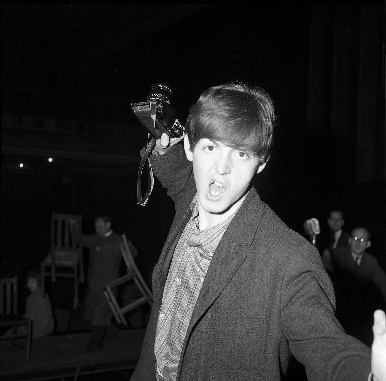 A black and white photo of Paul McCartney holding up a camera and making a face.