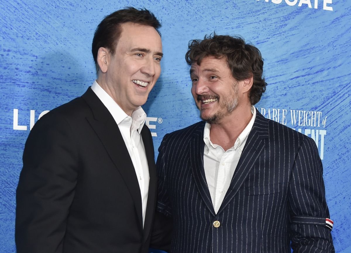 Nicolas Cage and Pedro Pascal pose together in front of a blue backdrop.