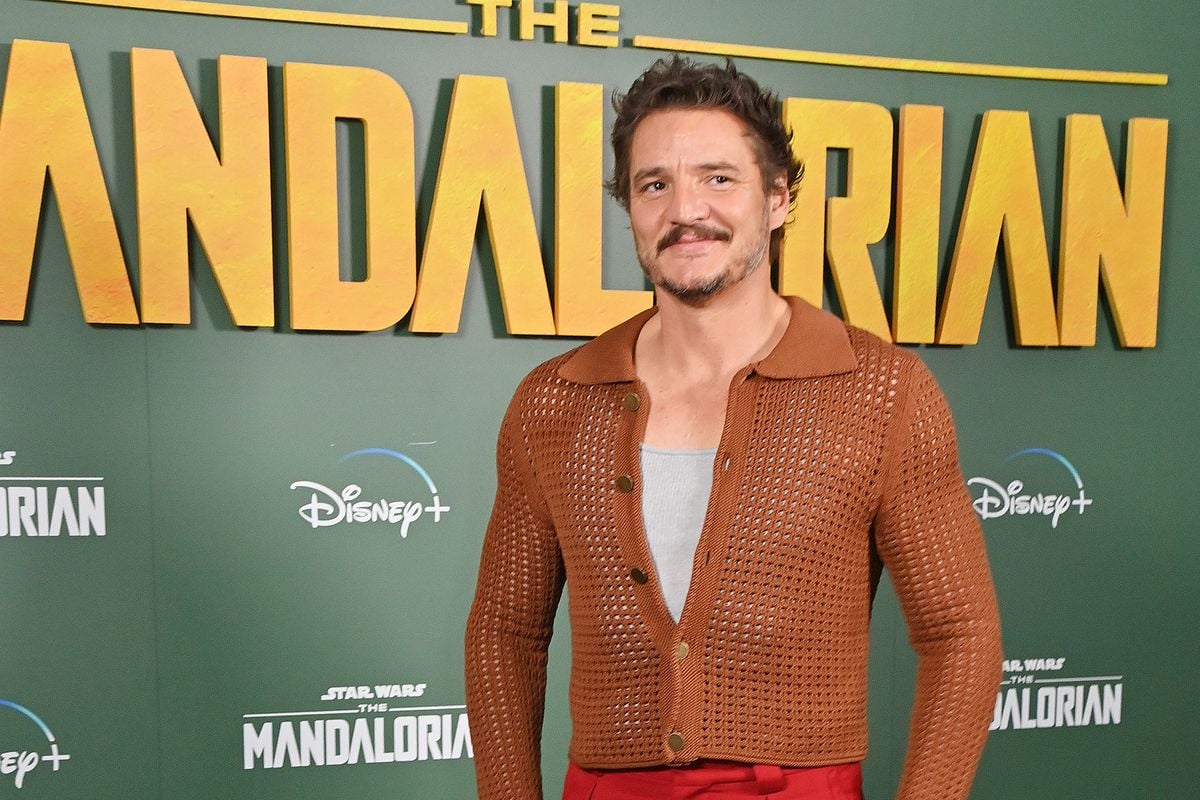 Pedro Pascal poses for photos in front of a backdrop featuring the logo for "The Mandalorian"