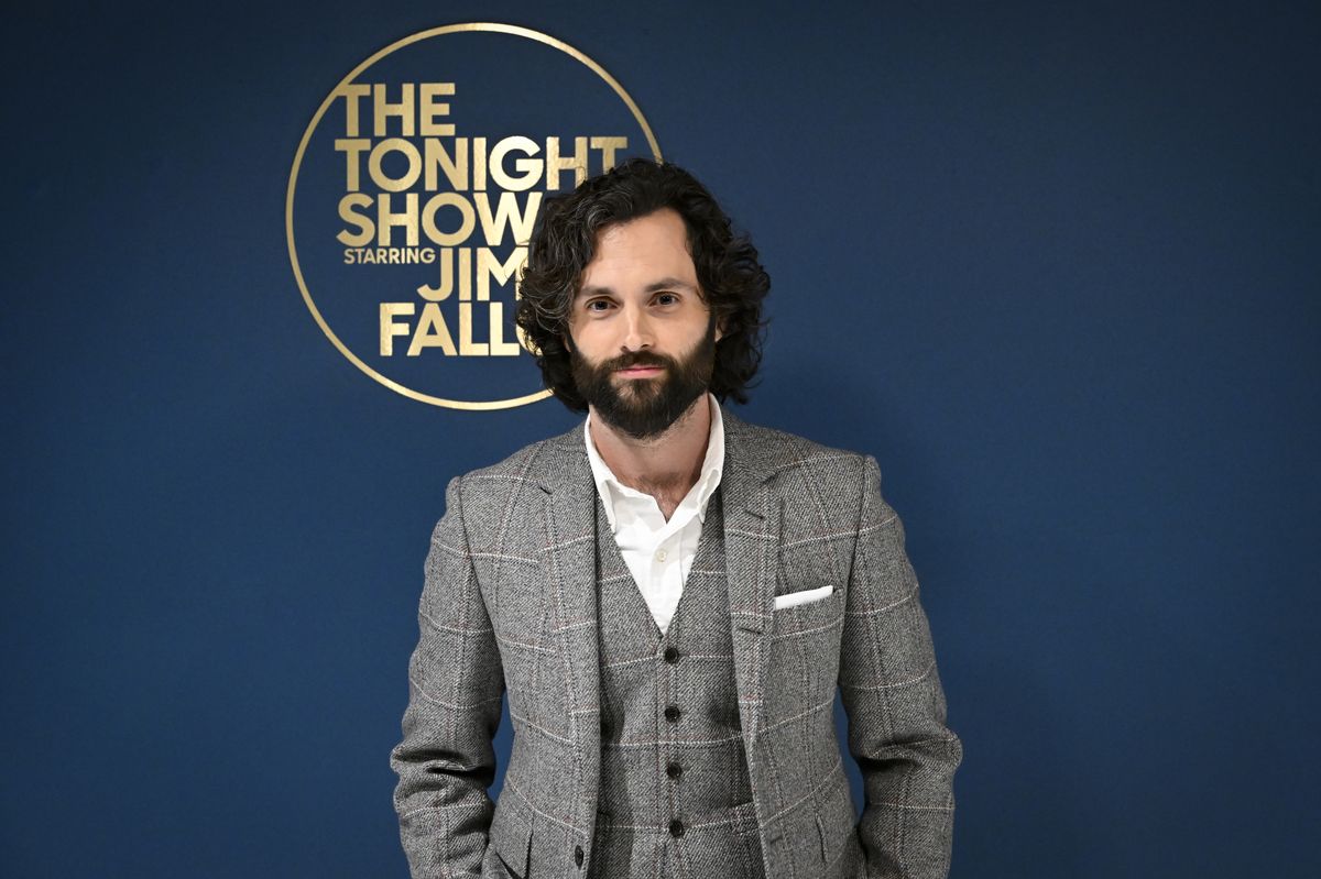 Actor Penn Badgley poses in front of a blue backdrop featuring the logo for "The Tonight Show With Jimmy Fallon"