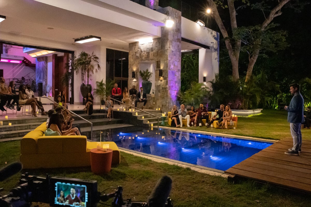 Nick Lachey and the Perfect Match contestants at their filming location in Panama City. The contestants sit around a pool while Nick stands in front of them.