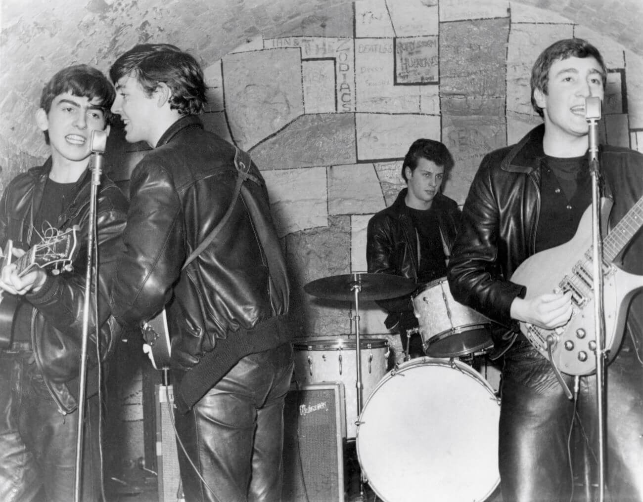 A black and white picture of George Harrison, Paul McCartney, Pete Best, and John Lennon performing together.