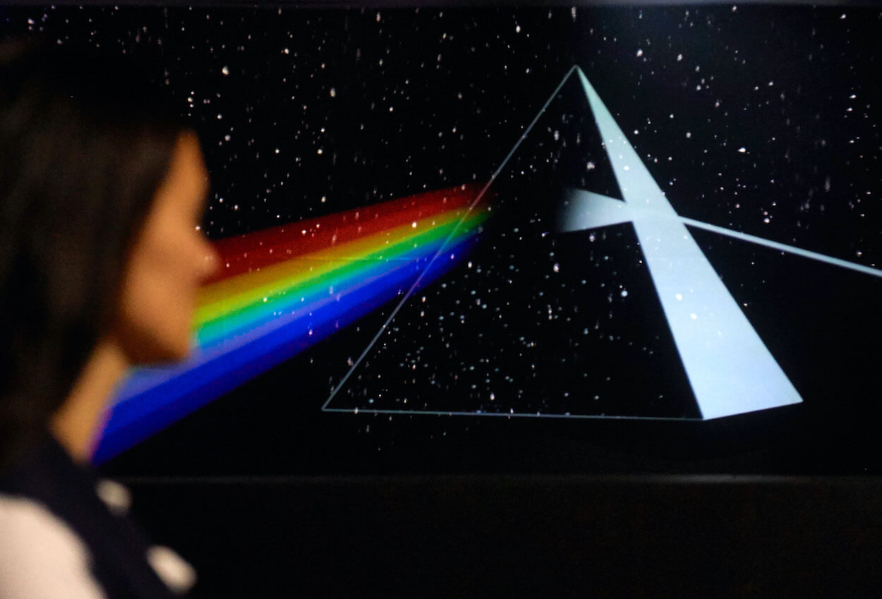 A woman walks past a display of a pyramid-shaped prism emitting a rainbow spectrum similar to the Pink Floyd album 'The Dark Side of the Moon.'