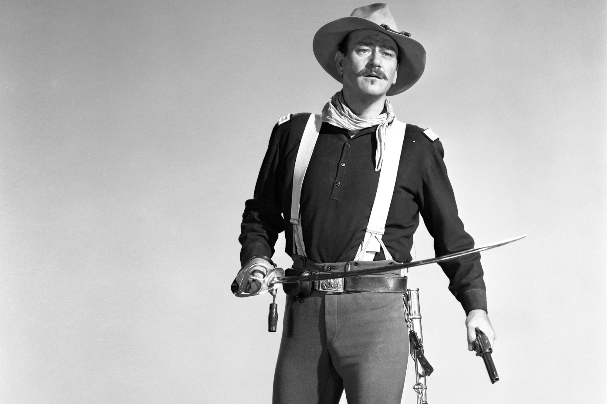 'Rio Grande' actor John Wayne as Lieutenant Colonel Kirby Yorke, whose fake sword ended up on 'Pawn Stars.' A black-and-white picture of him holding a sword and gun, while standing in a Western costume.