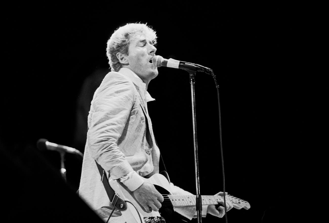 A black and white picture of Roger Daltrey playing guitar and singing into a microphone.