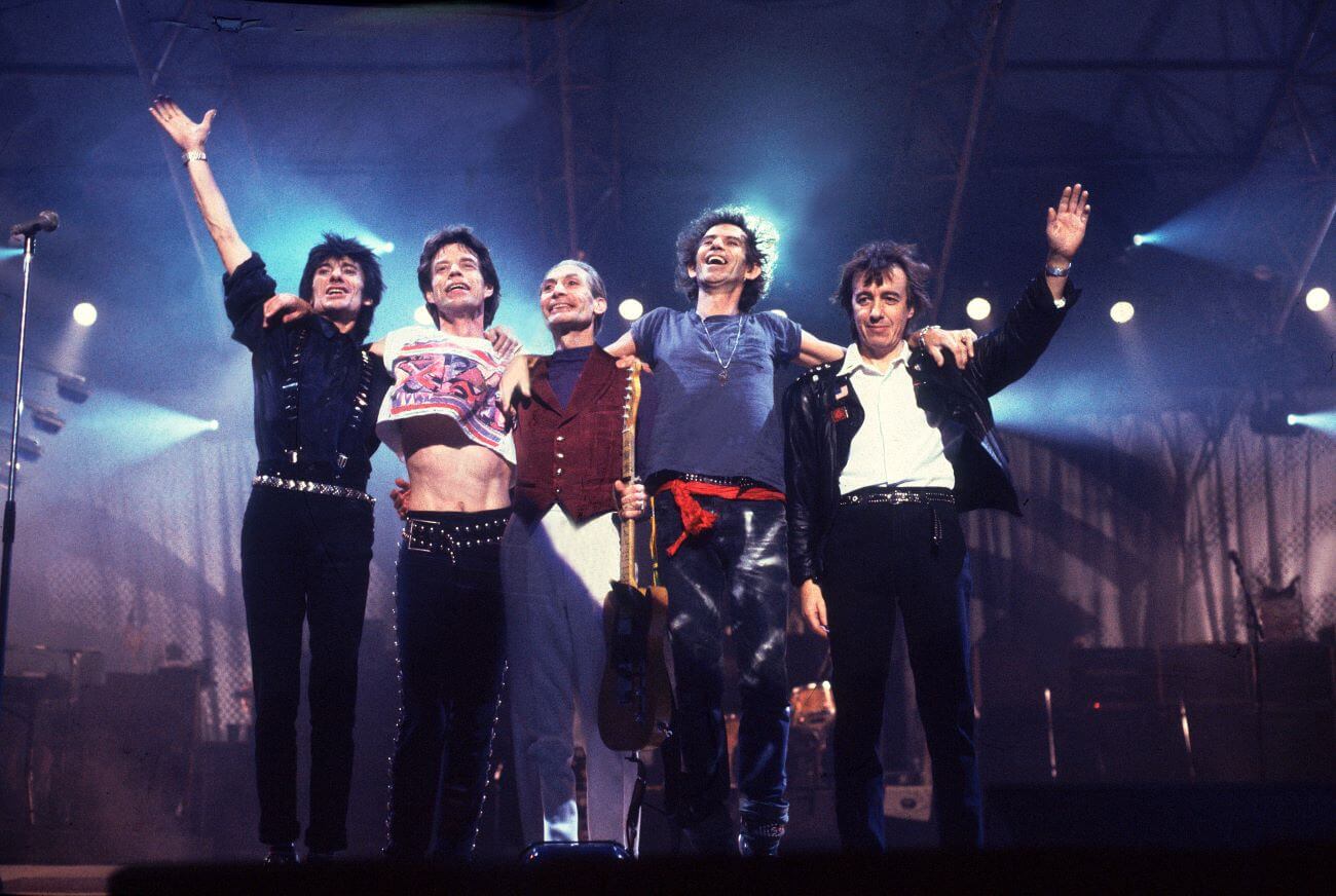 Ron Wood, Mick Jagger, Charlie Watts, Keith Richards, and Bill Wyman of The Rolling Stones posing together onstage. 