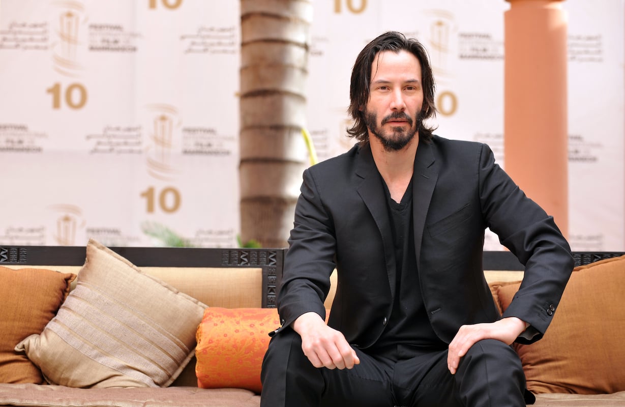 Keanu Reeves sits on a bench like his Sad Keanu meme