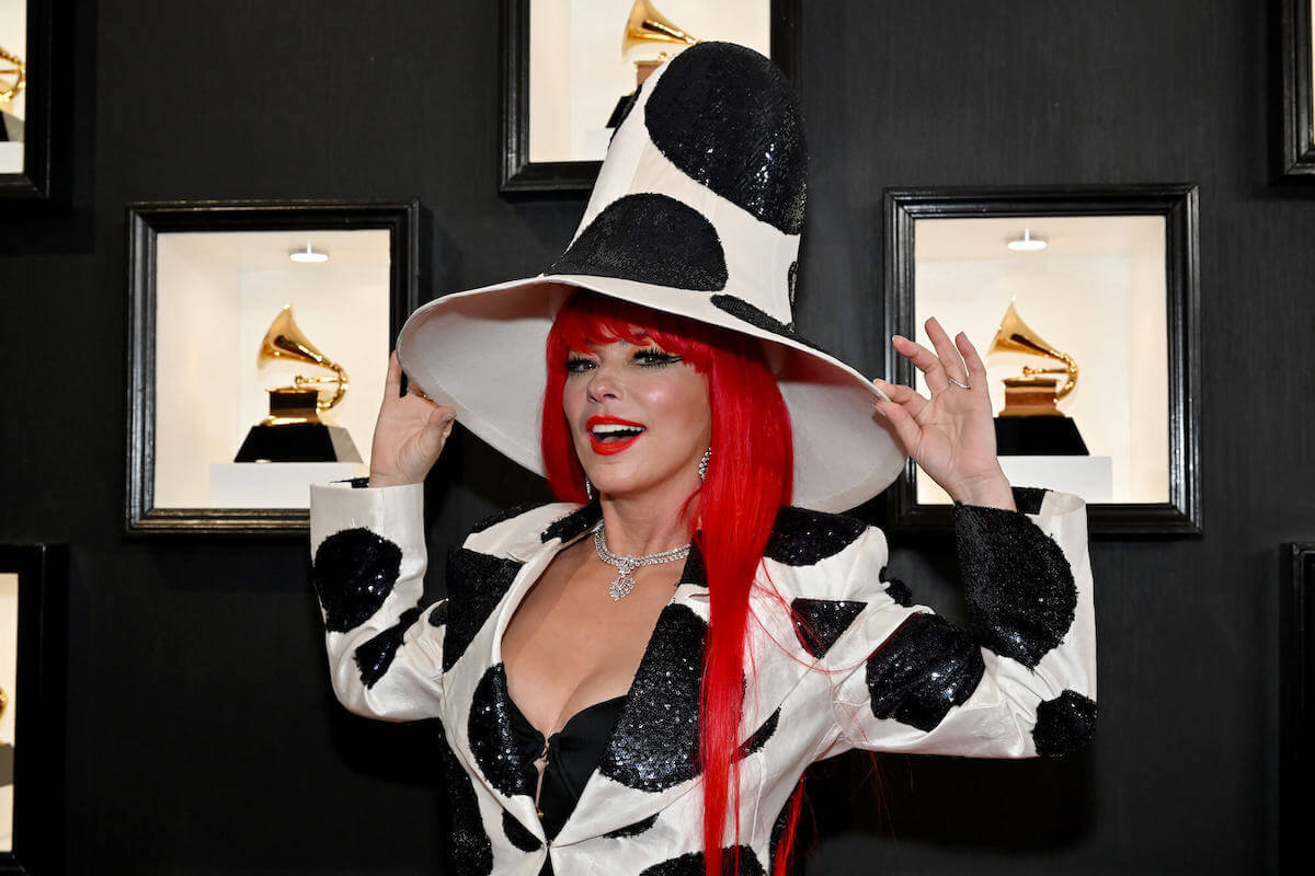 Shania Twain smiling, holding the brim of a large white hat with black polka dots