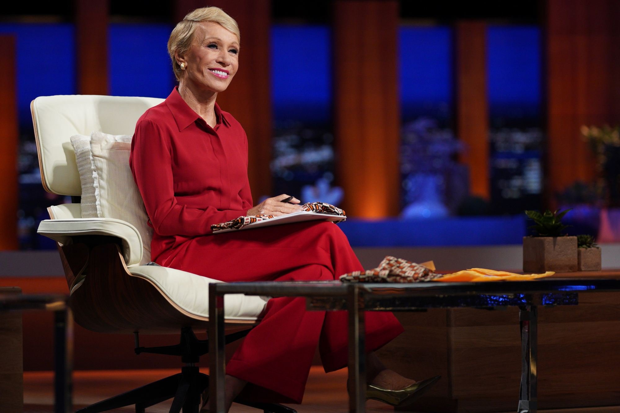 'Shark Tank' Barbara Corcoran smiling wearing a red suit, sitting in a white chair.
