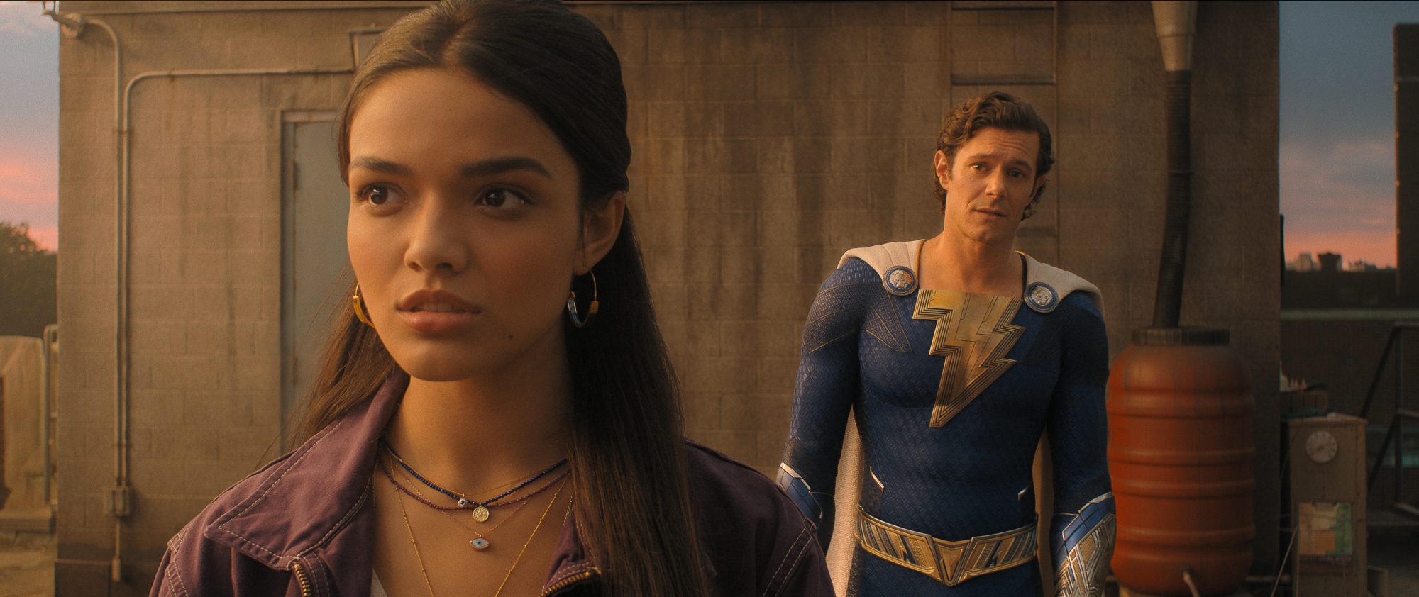 'Shazam! Fury of the Gods' Rachel Zegler as Anthea and Adam Brody as Super Hero Freddy. Zegler is facing the camera and Brody is standing behind her looking at her.