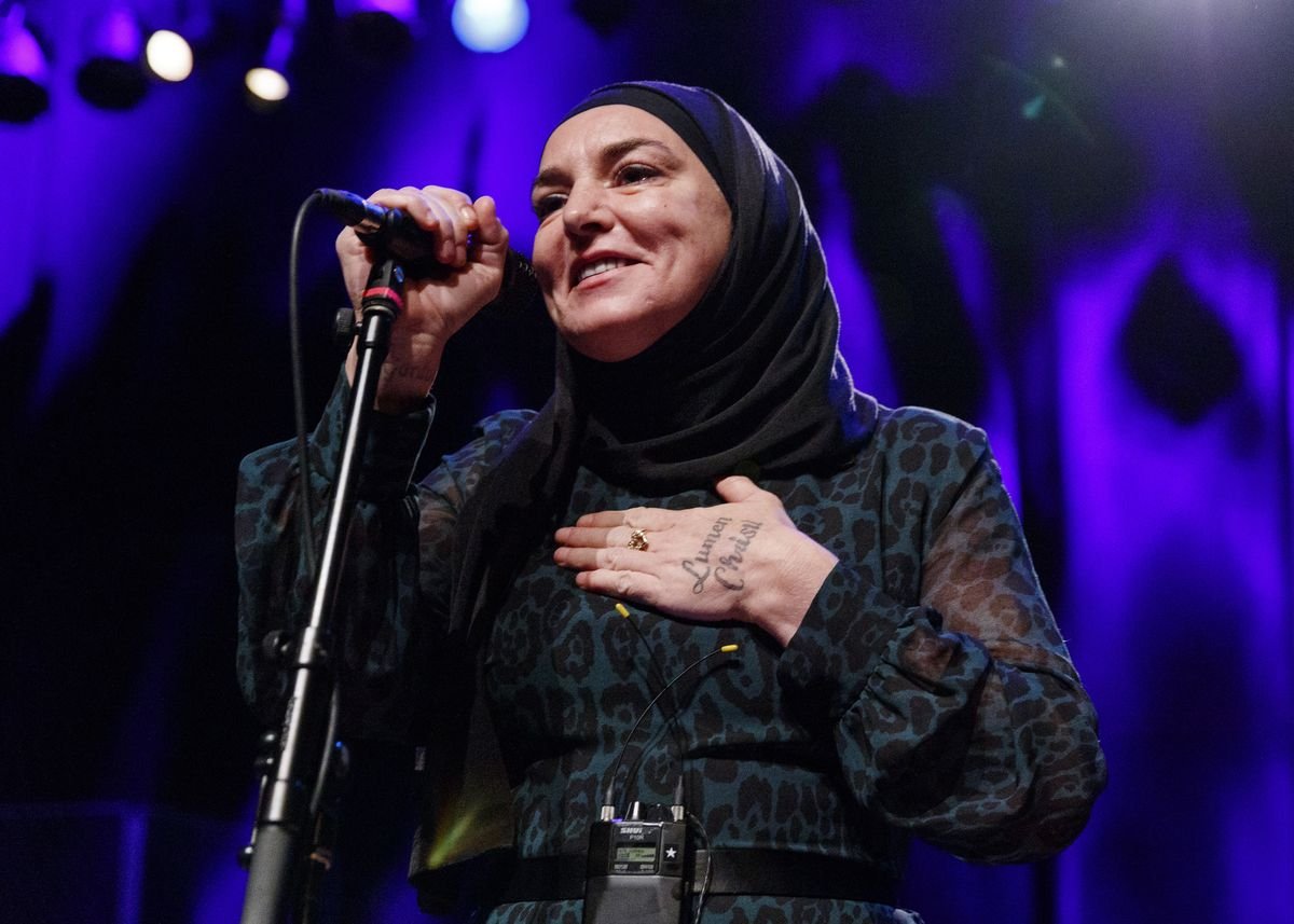 Sinead O'Connor smiles while holding a microphone.