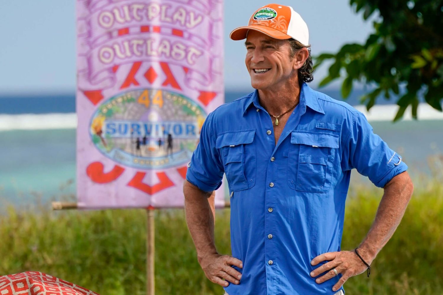 Jeff Probst, the host of 'Survivor 44' on CBS, wears a bright blue button-up shirt with rolled-up sleeves and an orange and white 'Survivor' baseball cap.