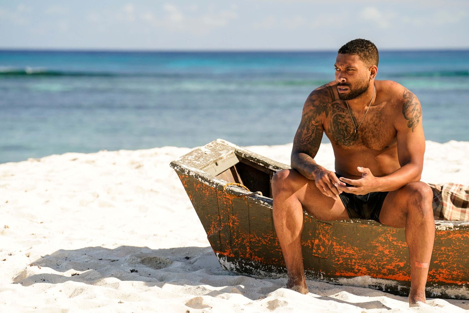 Brandon Cottom, who is competing in 'Survivor' Season 44 on CBS, wears black shorts while sitting on a small boat on the beach.