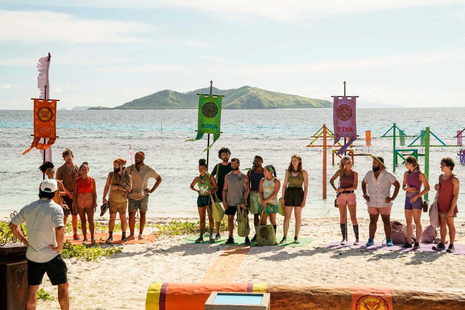 The Ratu, Soka, and Tika tribes stand on their respective mats on the beach and listen to host Jeff Probst, who recently gave away showmance spoilers, during a challenge in 'Survivor' Season 44 Episode 3, 'Sneaky Little Snake,' on CBS.