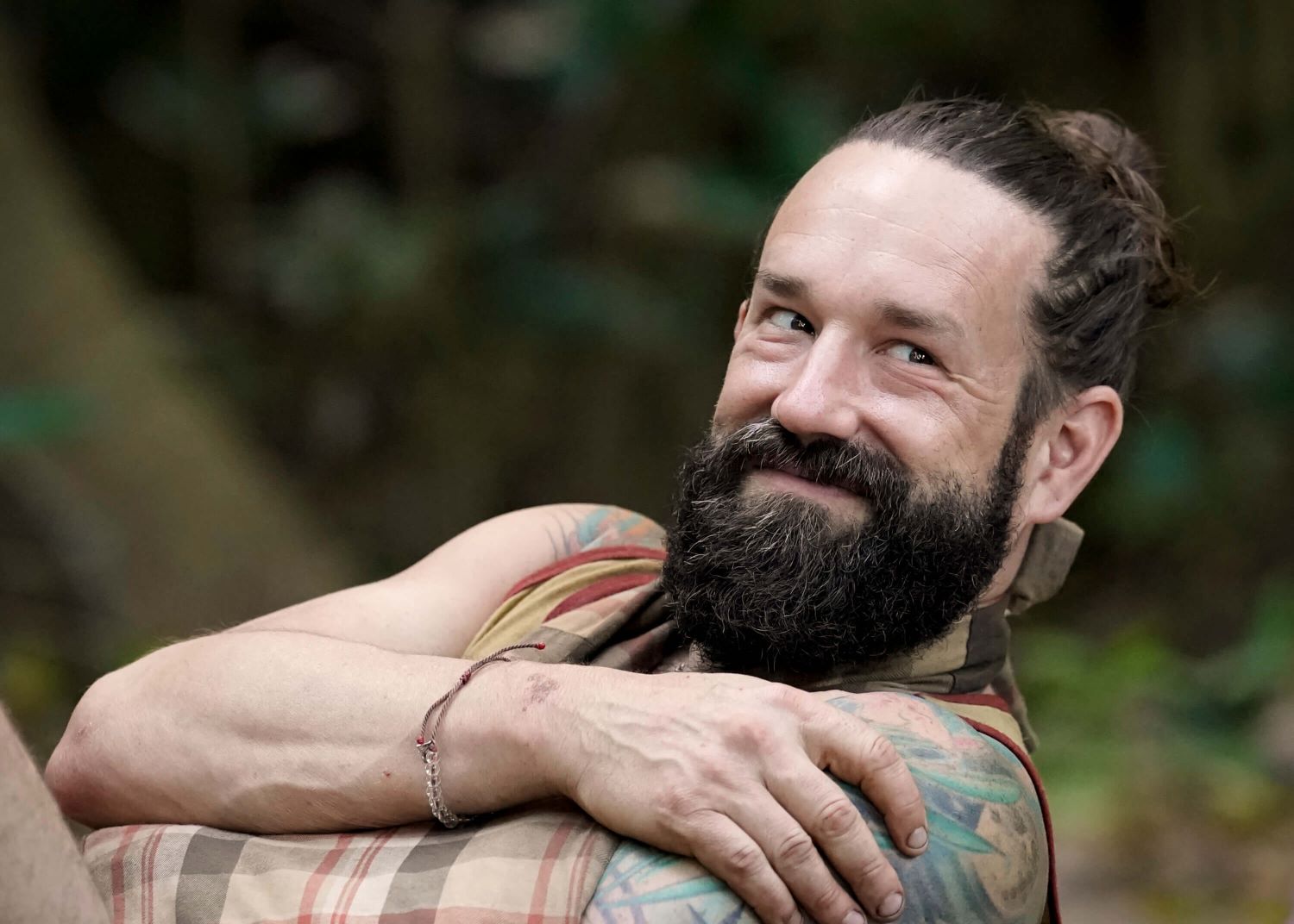 Matthew Grinstead-Mayle, a castaway on 'Survivor 44' on CBS, wears a light orange tank top and a orange and brown plaid sling for his arm.