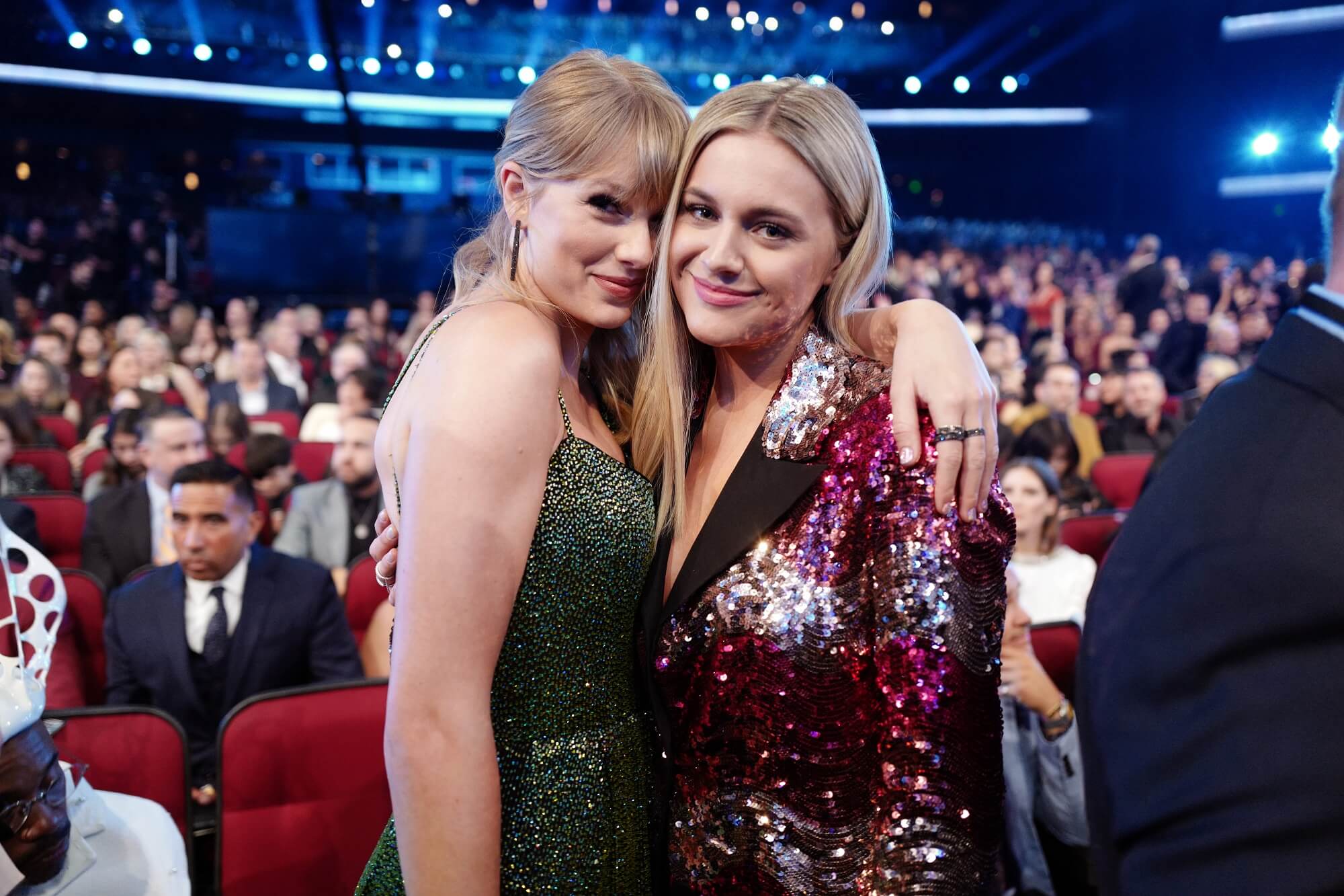 Taylor Swift and Kelsea Ballerini soft smile at the camera with their arms around each other