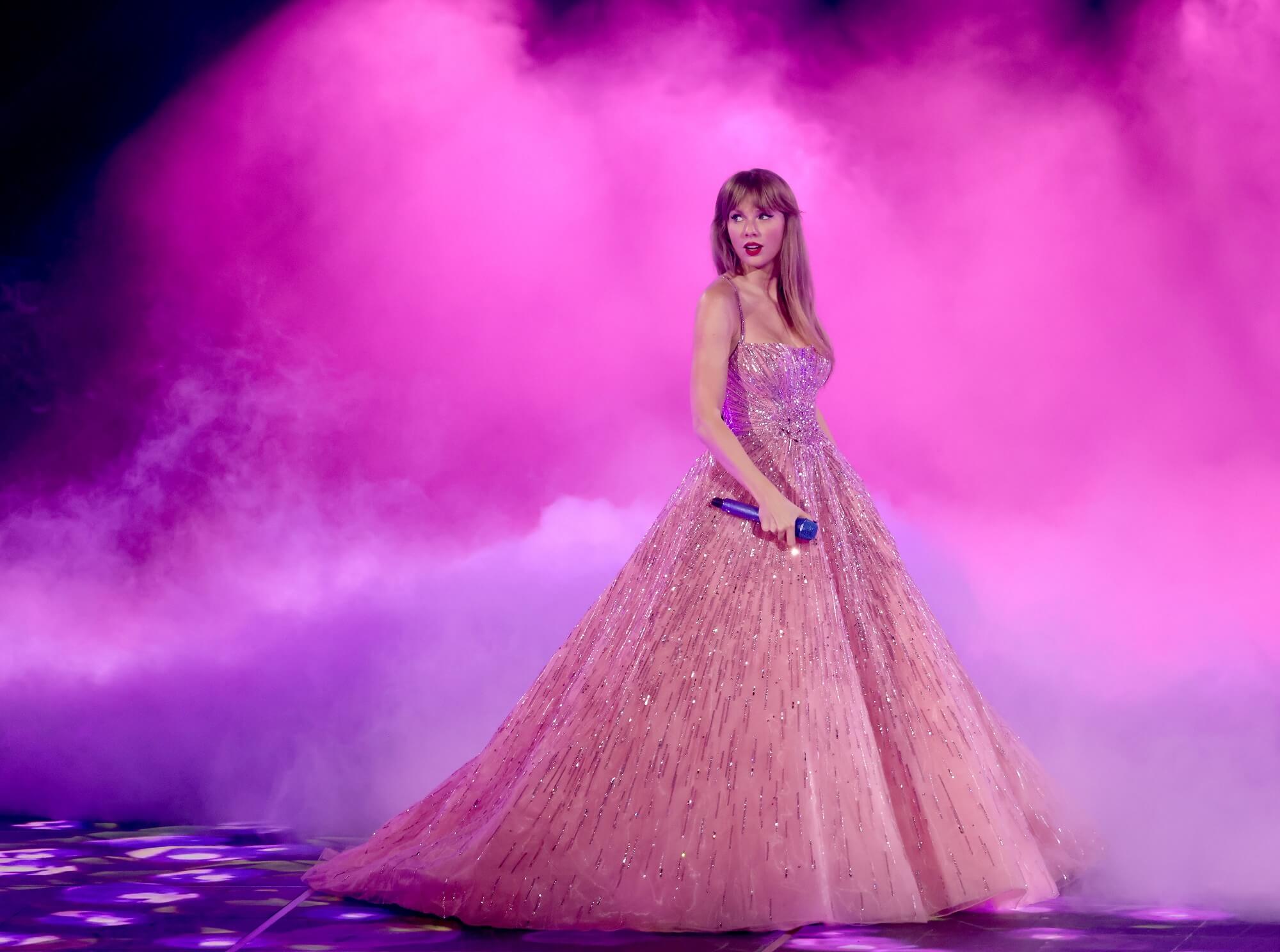Taylor Swift stands on stage in a pink ballgown surrounded by pink mist during 'The Eras Tour'