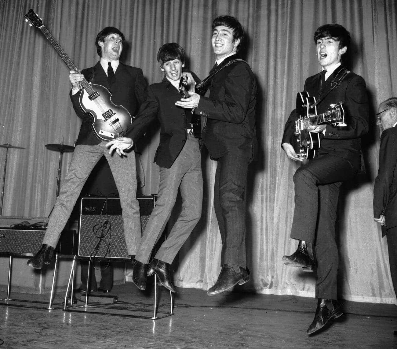 A black and white picture of Paul McCartney, Ringo Starr, John Lennon, and George Harrison wearing suits and jumping in the air on a stage.