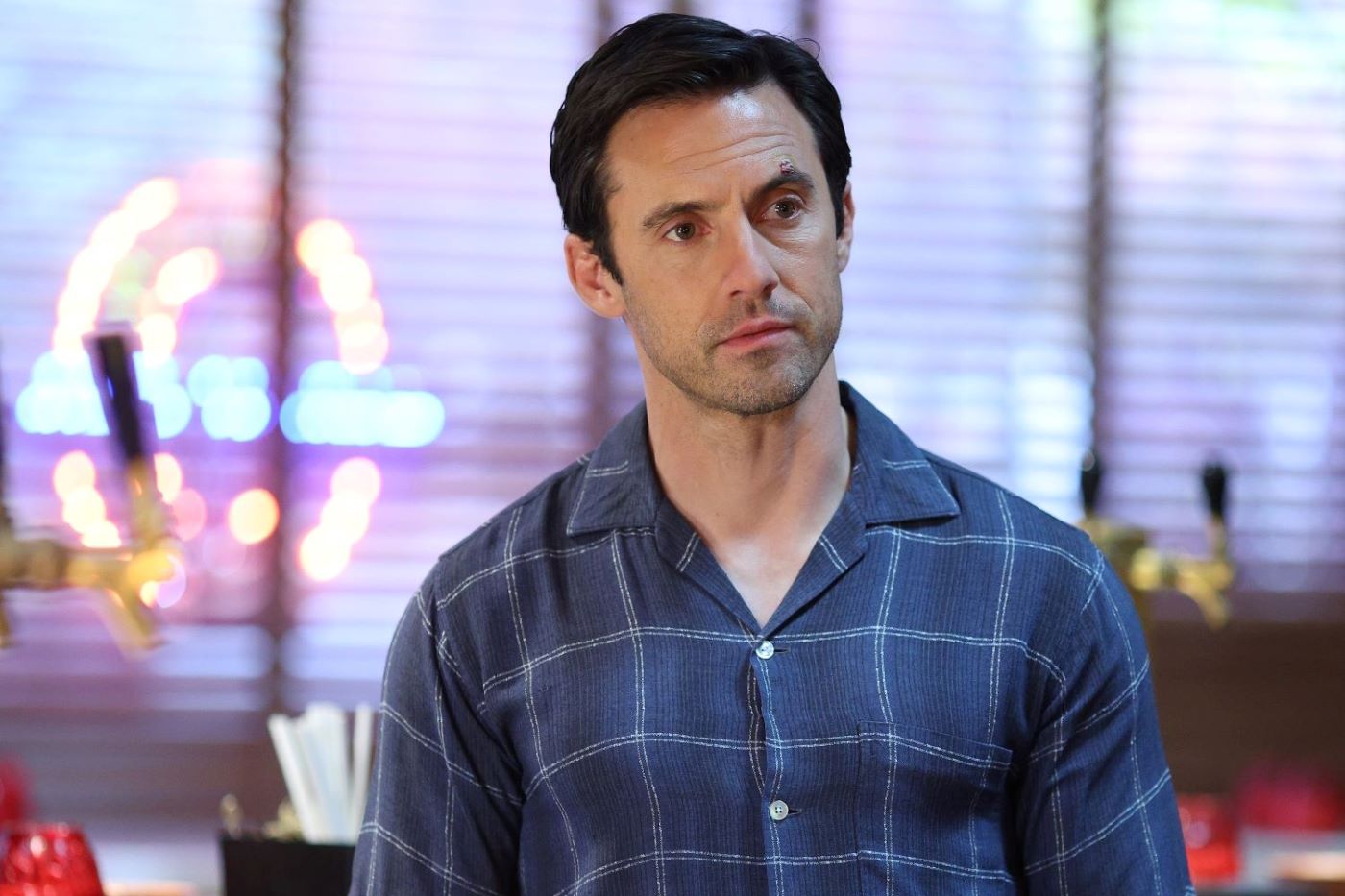 Milo Ventimiglia, in character as Charlie Nicoletti in 'The Company You Keep' Season 1 Episode 4, 'All In,' wears a blue button-up shirt with white horizontal and vertical intersecting stripes on it.