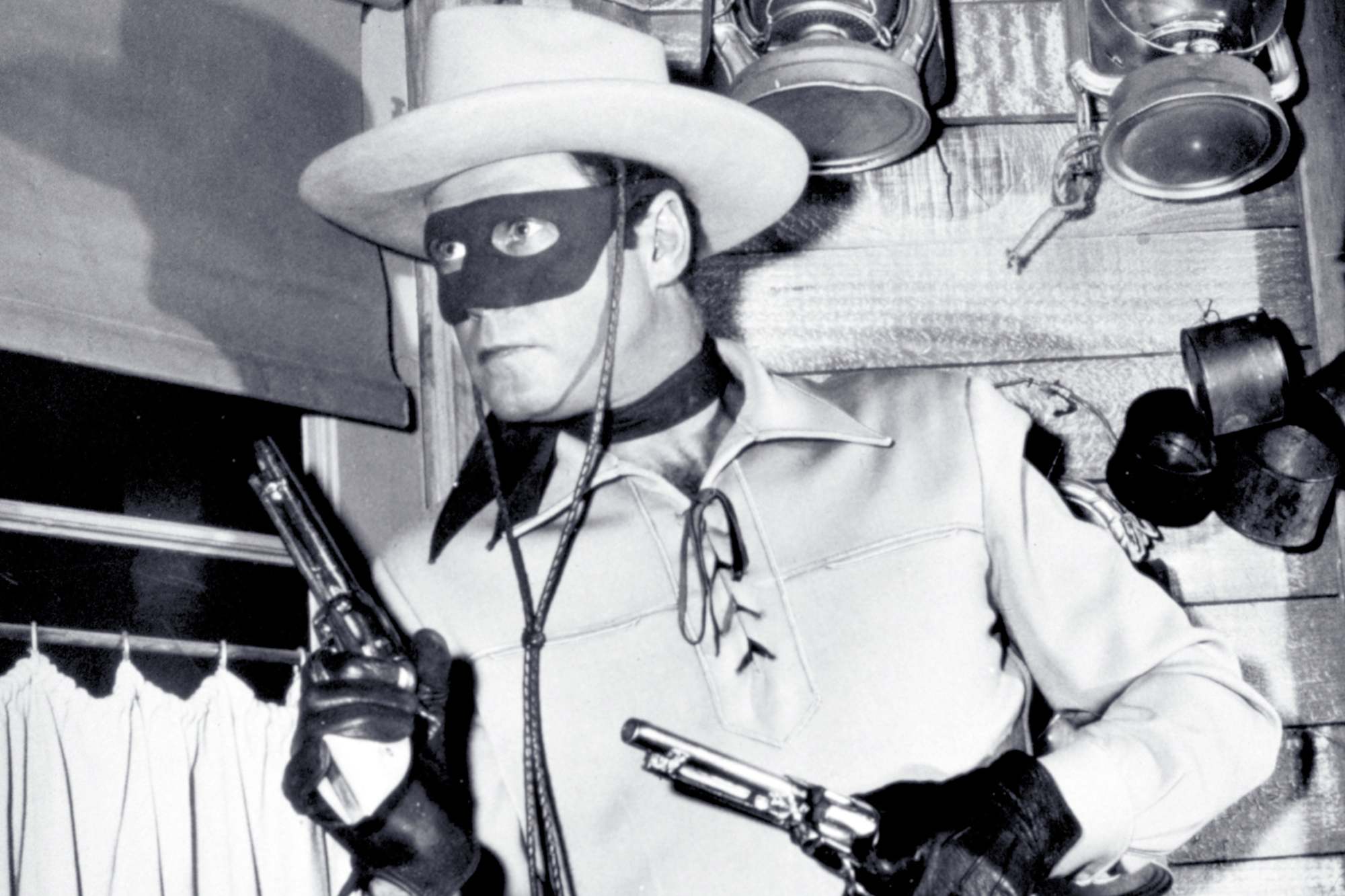 'The Lone Ranger' Clayton Moore as the Lone Ranger in script. He's holding two guns, wearing his mask and Western costume.