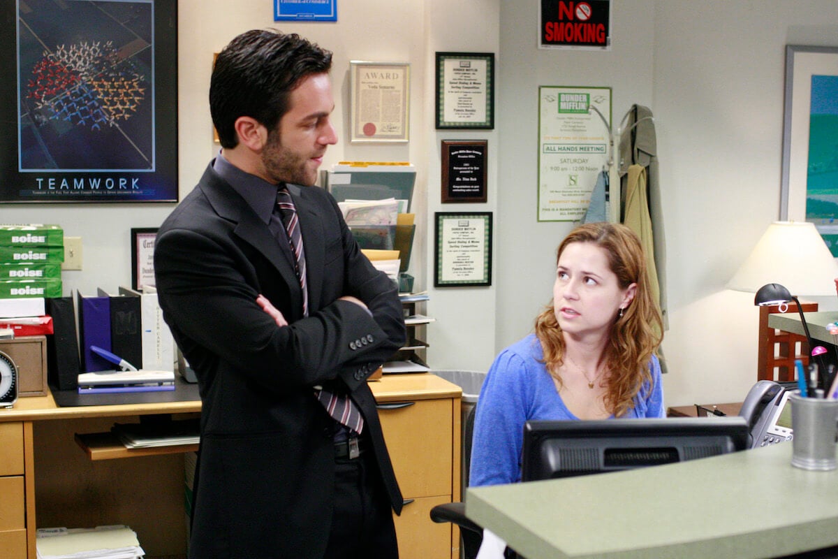'The Office' receptionist Pam (Jenna Fischer) sits at her desk while Ryan (B.J. Novak) stands folding his arms