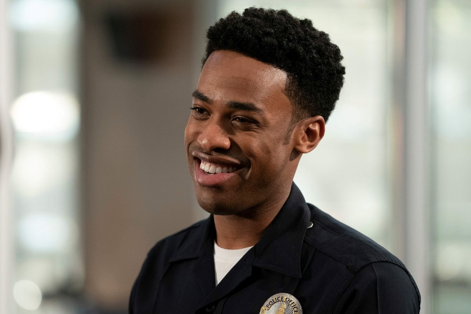 Titus Makin Jr, in character as Jackson West in 'The Rookie' on ABC, wears his dark blue police uniform over a white shirt.