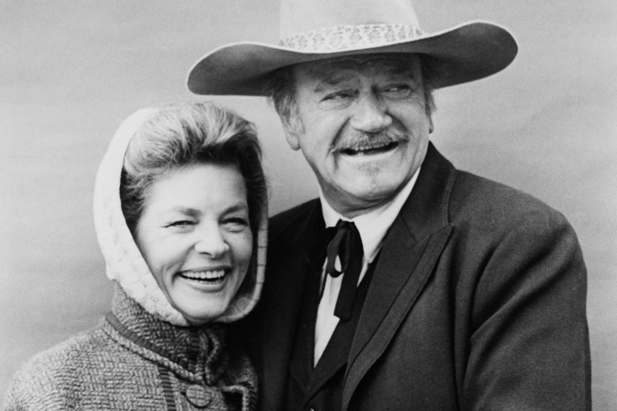 'The Shootist' Lauren Bacall as Bond Rogers and John Wayne as J.B. Books in a black-and-white picture, smiling next to each other in costume.