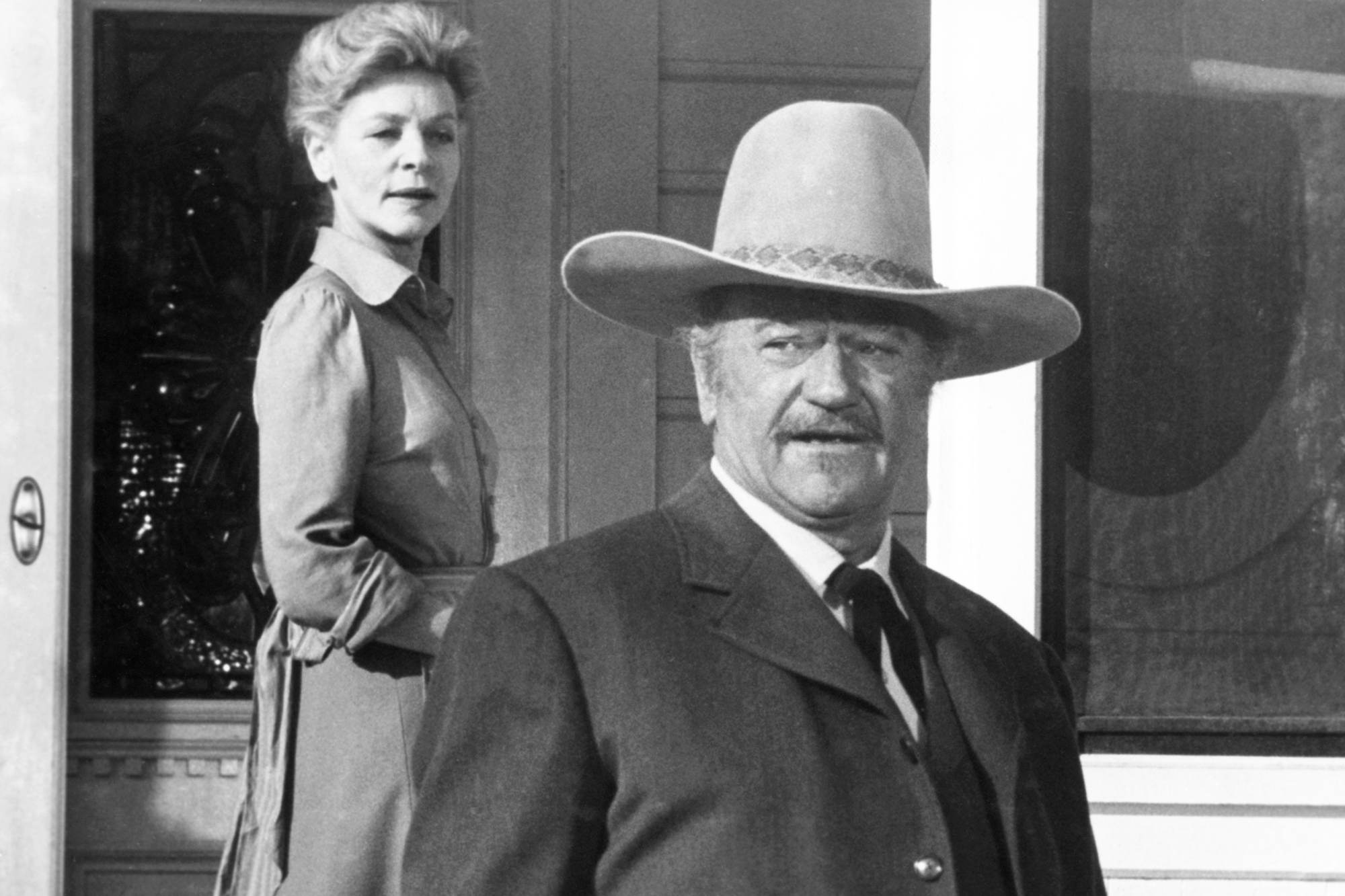 'The Shootist' Lauren Bacall as Bond Rogers and John Wayne as J.B. Books. Rogers is standing behind Books on the porch of the house.